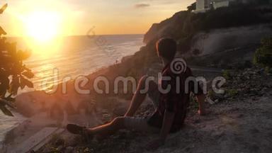 人类旅行者坐在岩石上，欣赏日落的海景。 徒步旅行者坐在大石头上，放松并欣赏风景